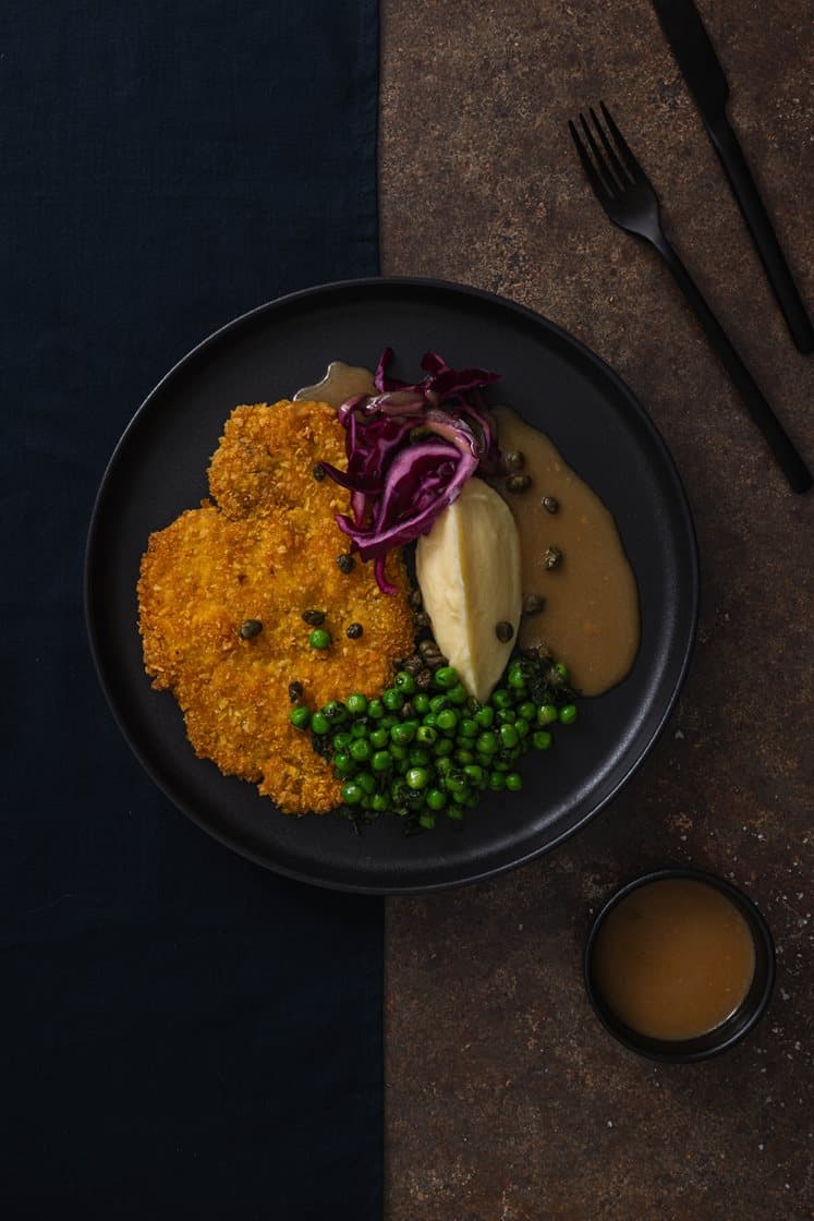 Svineschnitzel og potetkrem, servert med mynteerter og sjysaus med sprøstekte kapers