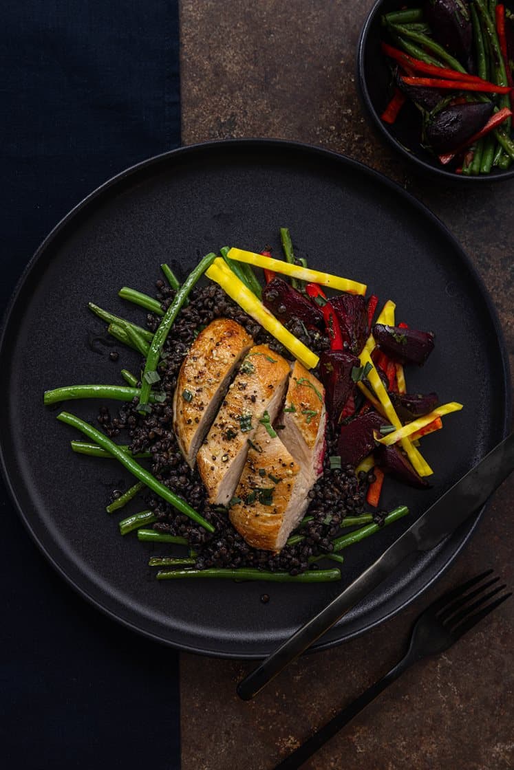 Pannestekt kyllingbryst og belugalinse-cassoulet, servert med bakte beter og trøffelsmør 