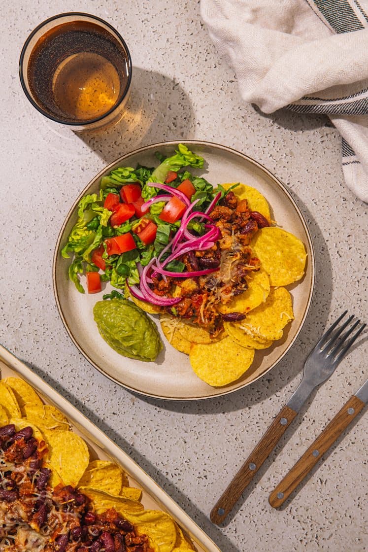 Ostegratinerte nachos med chili con carne, toppet med syltet rødløk, salat og guacamole